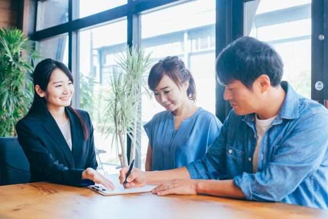 若い男女に契約を進めるスーツ姿の女性