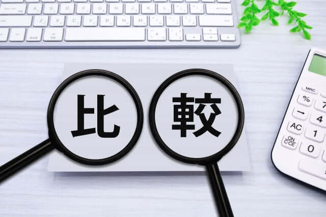 キーボード・電卓が置かれた机に比較と書かれた紙があり、虫眼鏡で拡大している。