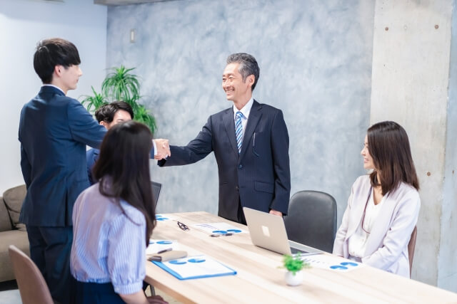 会議室でビジネスマン同士が笑顔で握手している